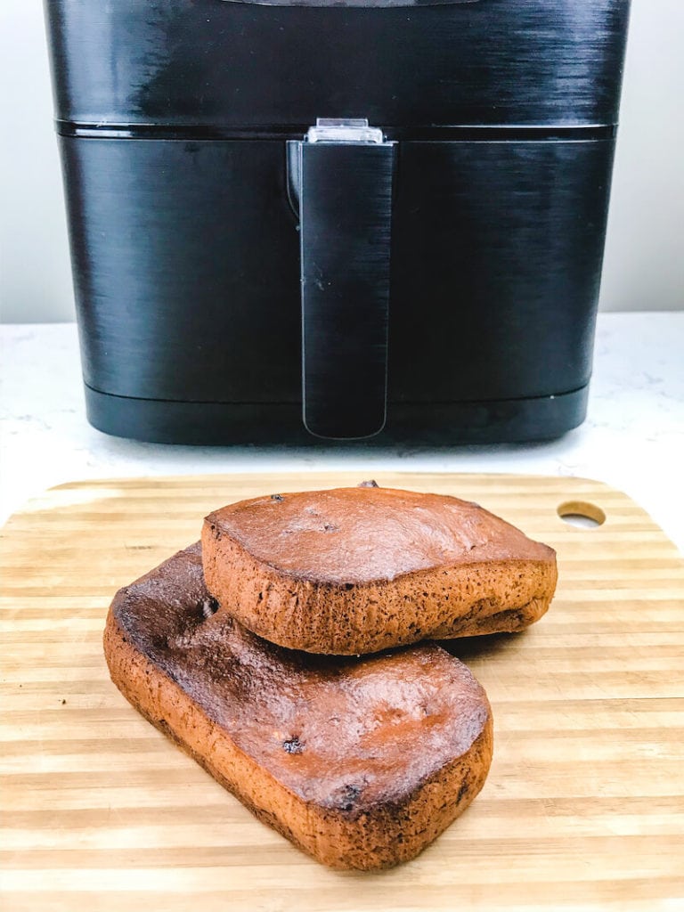Two loaves of banana bread stacked up on wooden cutting board in front of air fryer