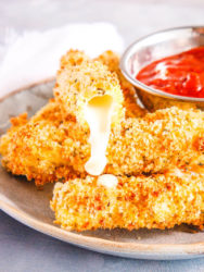 A plate of mozzarella sticks with one cut in half and cheese oozing out.