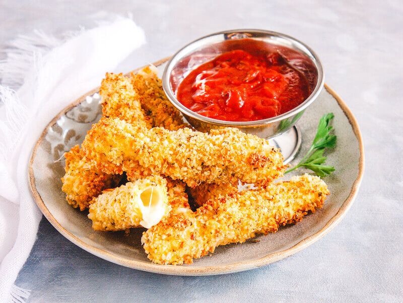 A grey plate of mozzarella sticks next to a small metal dish of marinara.