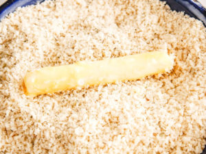 Cheese stick being dredged in breadcrumbs.