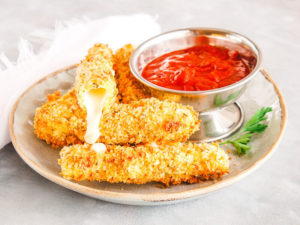 A grey plate full of mozzarella sticks with one mozzarella stick on top showing the inside with melted cheese coming out.