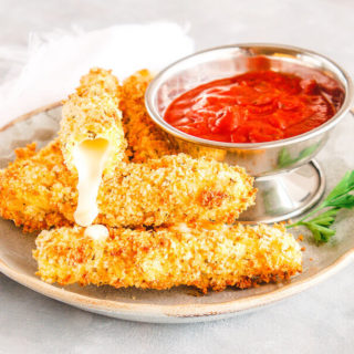 A grey plate full of mozzarella sticks with one mozzarella stick on top showing the inside with melted cheese coming out.