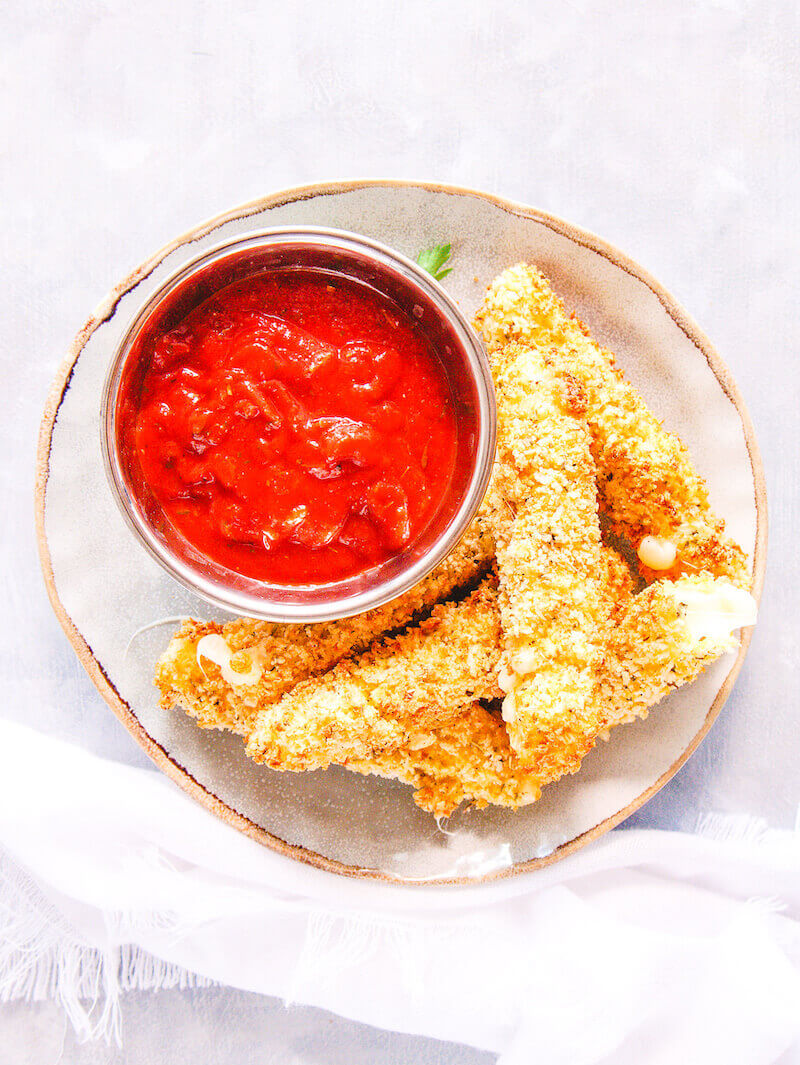 Overhead picture of mozzarella sticks and marinara sauce on a small grey plate.