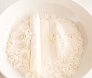 A cheese stick inside a bowl of flour.