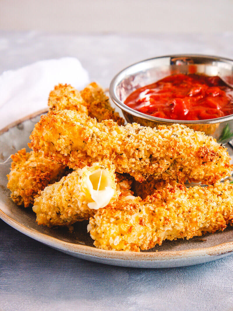 A plate of 6 homemade mozzarella sticks with a metal dish of marinara sauce.