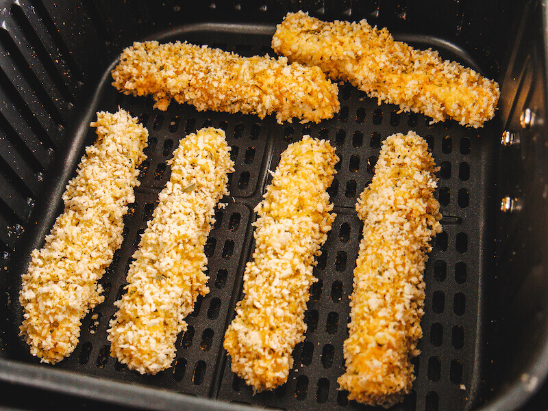 Coated cheese sticks inside basket of air fryer.