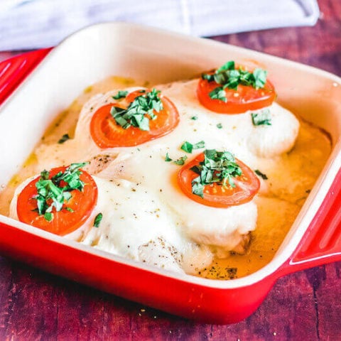 A red baking dish filled with 4 pieces of chicken caprese.