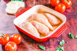4 chicken breasts inside a red baking dish and coated with olive oil and seasoning.