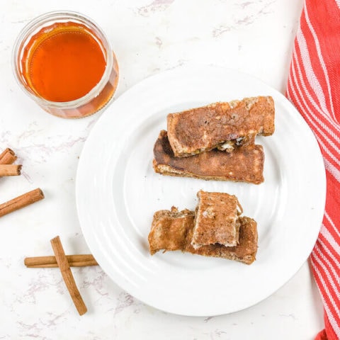 A white plate of French toast sticks next to cinnamon sticks on the counter.