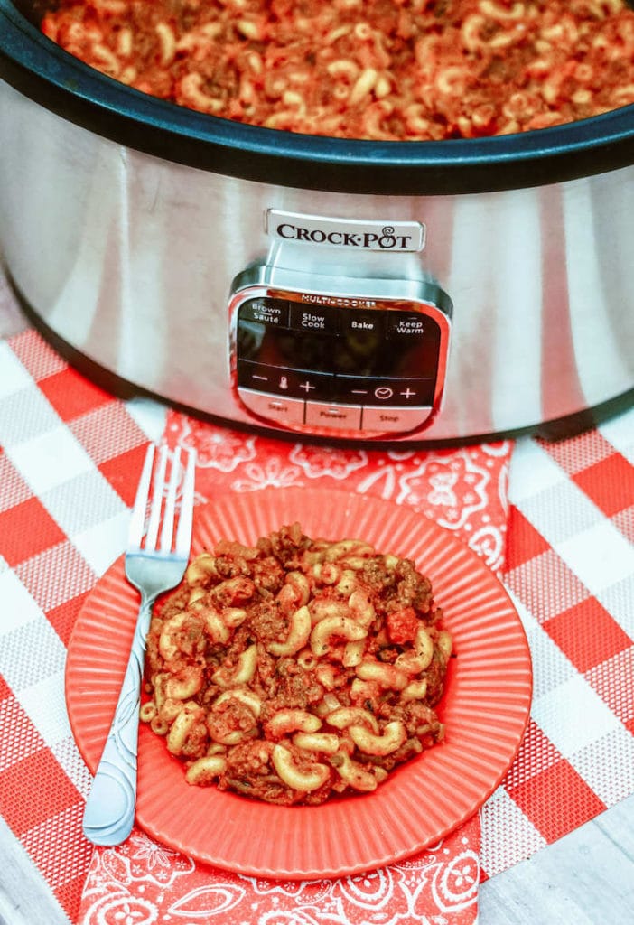 A plate of goulash in front of a crockpot filled with American goulash.