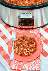 A plate of goulash in front of a sliver crockpot.