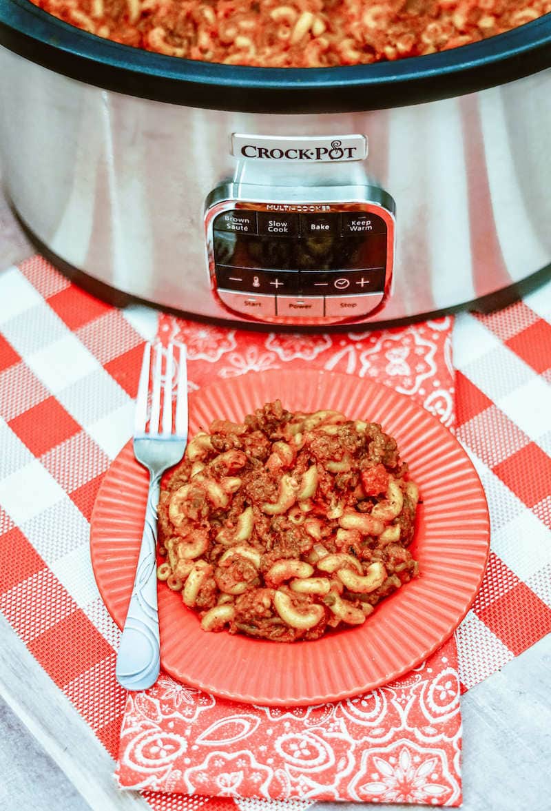 A plate of goulash in front of a sliver crockpot.