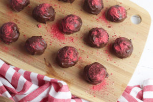 Truffles dusted in strawberry powder on a wooden cutting board.