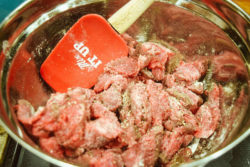 Sliced steak in a bowl mixed with flour.