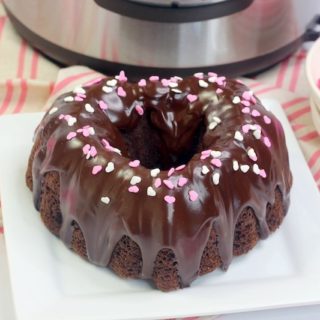 A chocolate cake shaped like a heart with pink heart sprinkles on top.