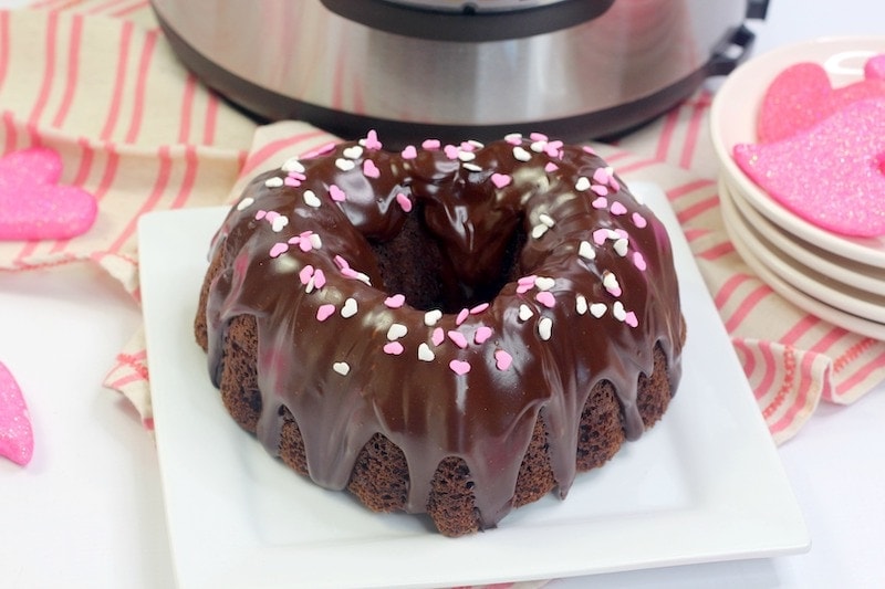 A chocolate cake shaped like a heart with pink heart sprinkles on top.