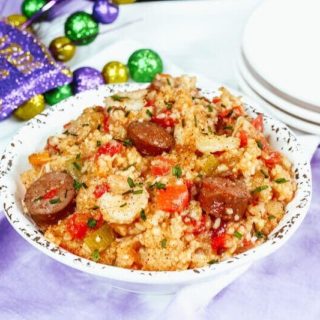 A white bowl filled with jambalaya next to Mardi Gras decorations in purple, gold, and green.