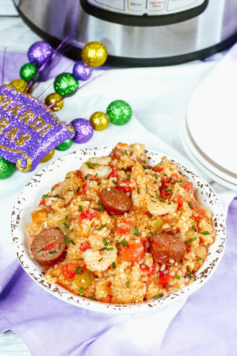 A bowl of jambalaya in a white and grey bowl in front of an instant pot.
