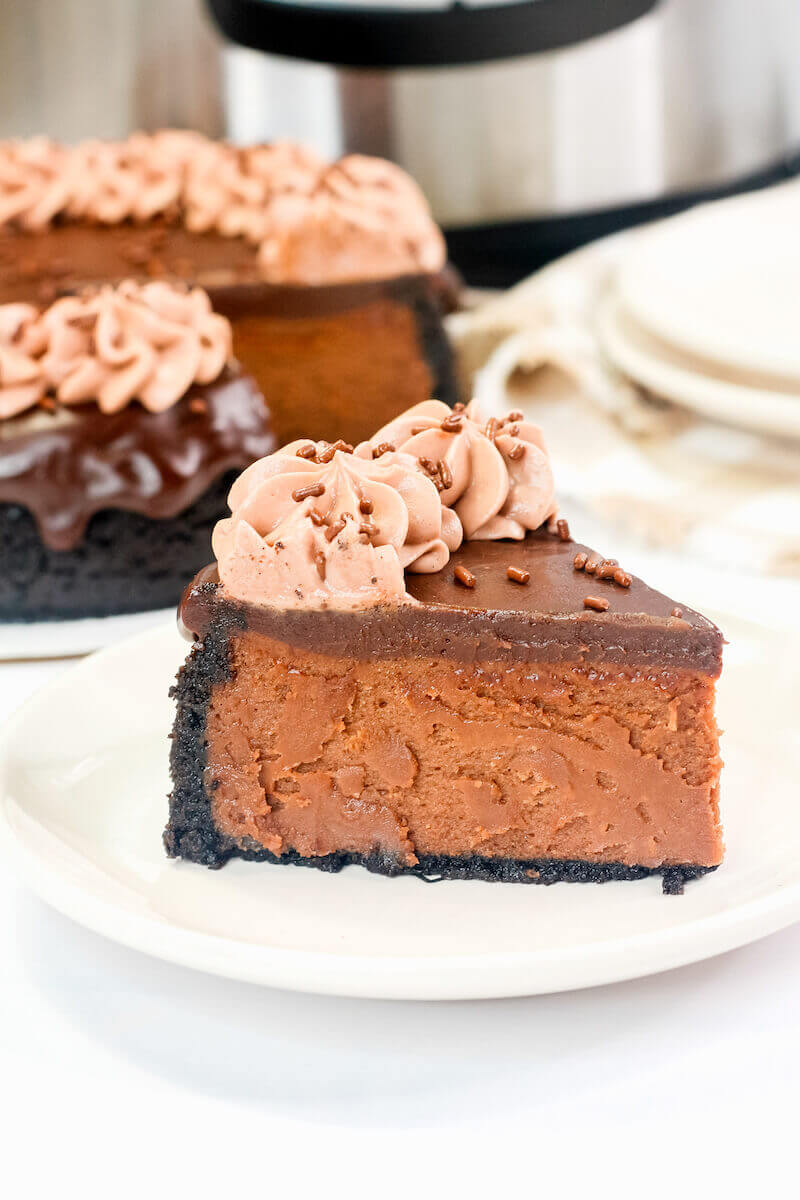 A slice of nutella cheesecake on a white plate with chocolate whipped cream and sprinkles on top.