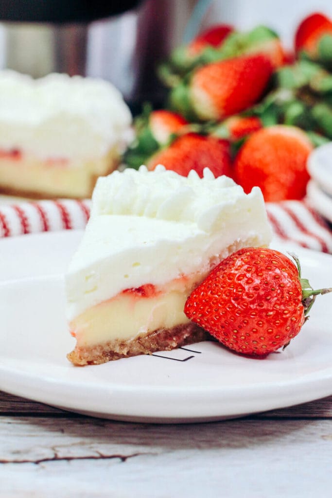 A slice of strawberry cheesecake on a white plate with a strawberry next to it.