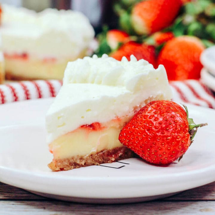 A pile of strawberries behind a slice of strawberry cheesecake.