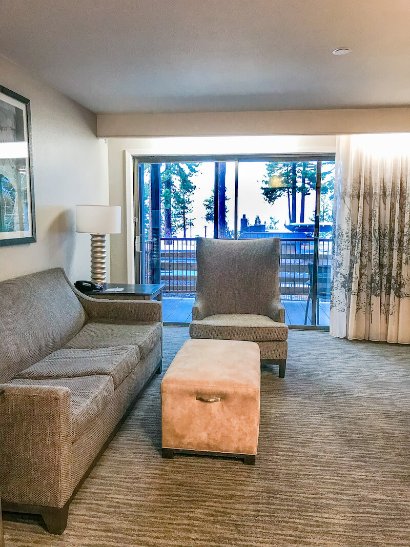 A family room with a grey couch and chair and views of Lake Tahoe in the window in the background.