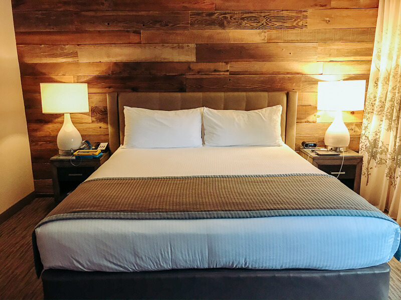 A king sized bed with a modern wood paneling on the wall behind it.