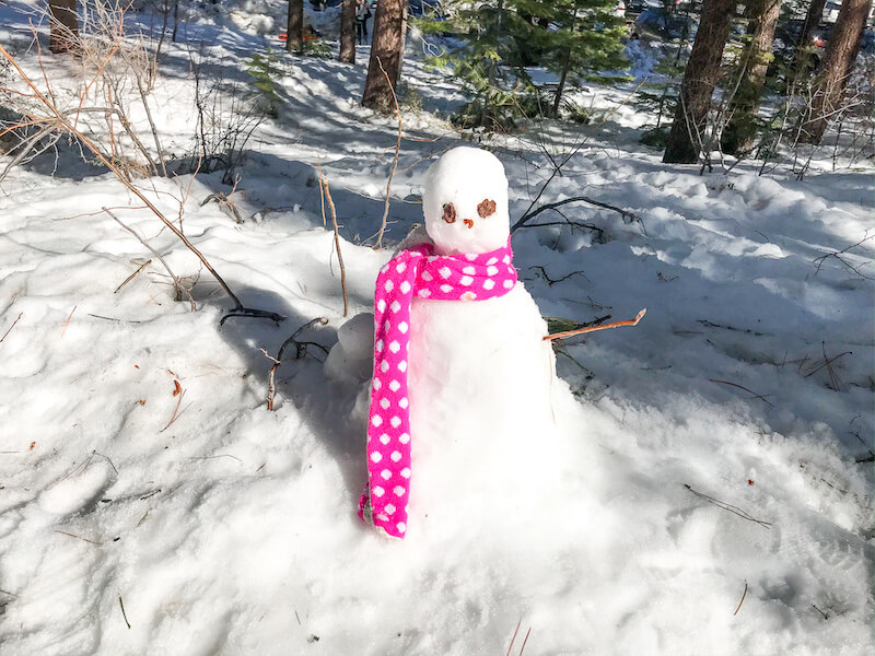 A snowman with a pink polkadot scarf around its neck.