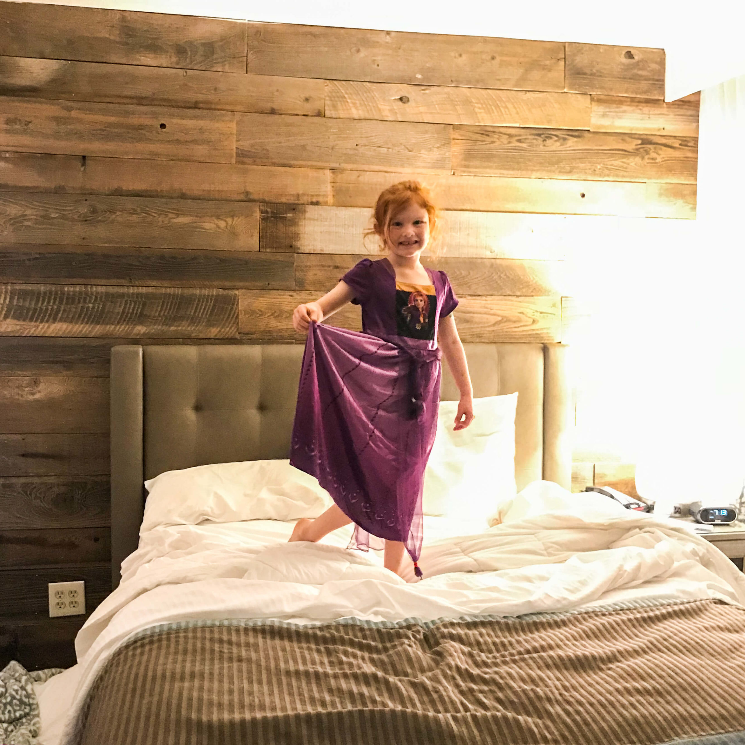 A little girl in a princess nightgown standing on a bed.