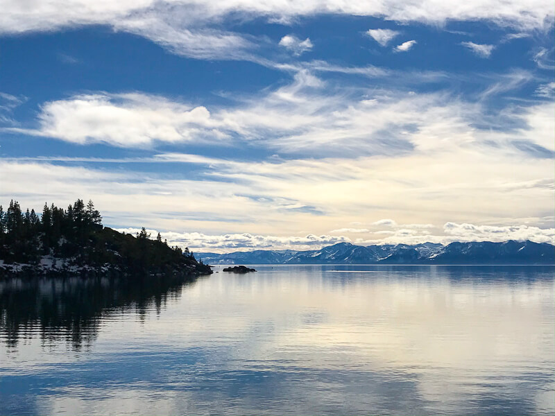 A picture of blue Lake Tahoe with clouds in the sky and trees in the distance on the left.
