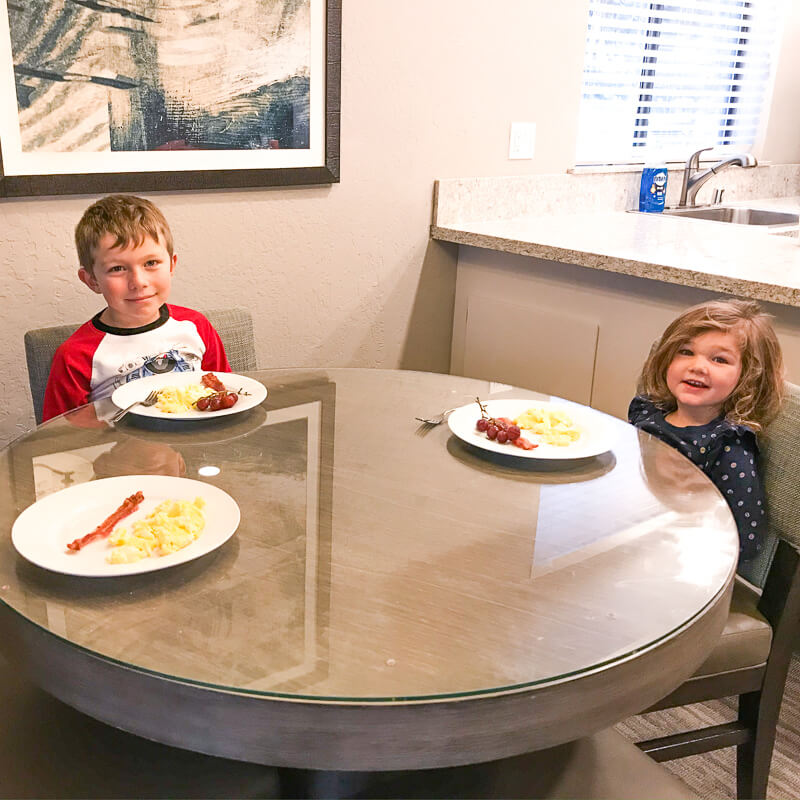 Two kids sitting at a table with plates of bacon and eggs in front of them.