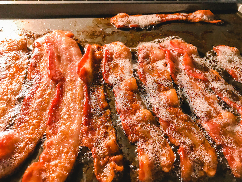 A pan of sizzling bacon inside an oven.
