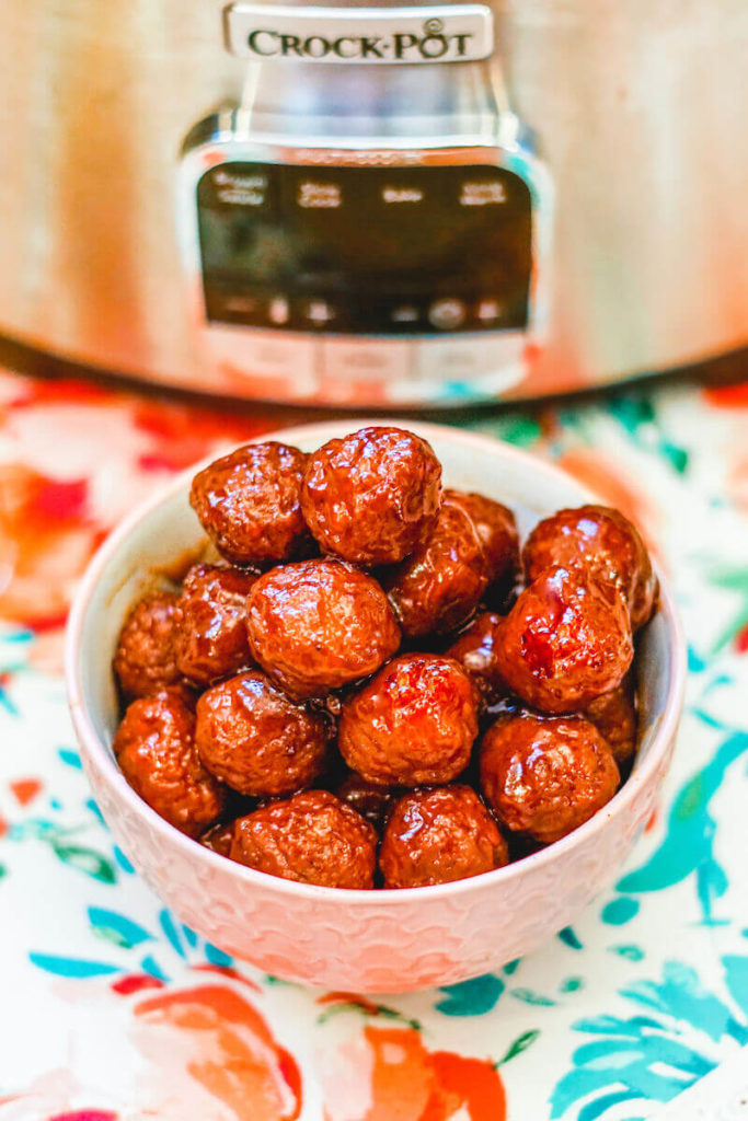 Close up of grape jelly meatballs in a white bowl, on top of a floral place mat.