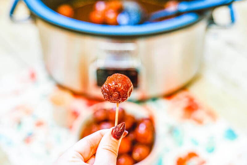 A hand holding up a grape jelly meatball on a toothpick.