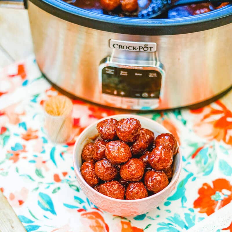 A bowl of cocktail meatballs in front of a crock pot full of meatballs.