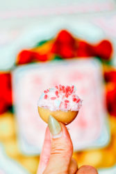 A hand holding up a cookie dipped in strawberry dunkaroo dip with sprinkles.