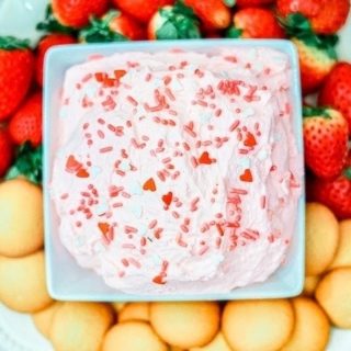 A white plate filled with strawberries, vanilla cookies, and a square bowl of strawberry cake batter dip in the center.