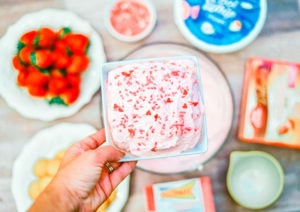 A hand holding up a square bowl of the cake batter dip covered in red sprinkles.