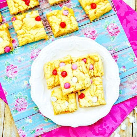 A pink tablecloth topped with a floral placemat with a cooling rack of cookie bars and a white plate of cookie bars on top!