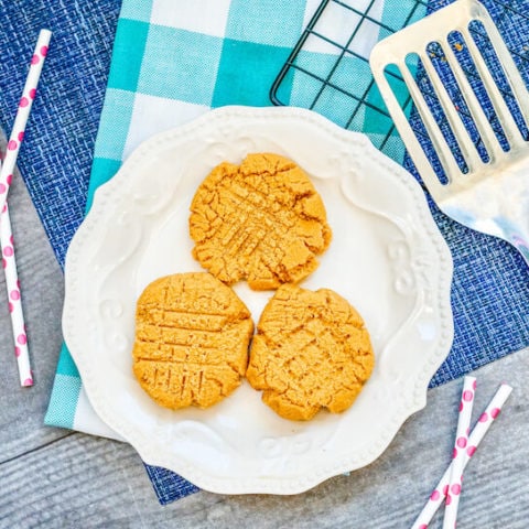 A white scalloped plate with three peanut butter cookies on it.