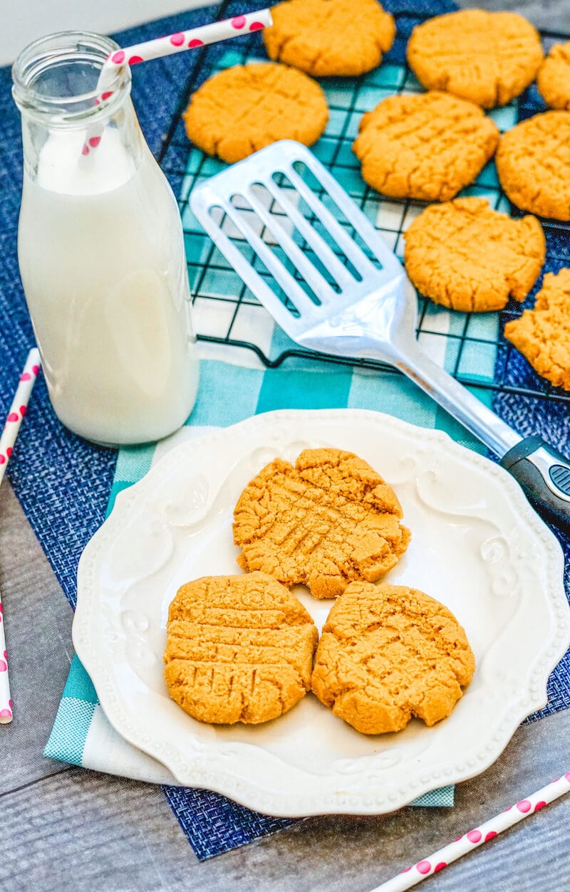 Bottle of milk next to a pretty white plate with three peanut butter cookies.
