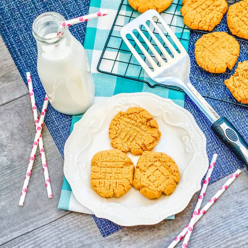 A plate of cookies next to a spatula, bottle of milk, and red and white straws.