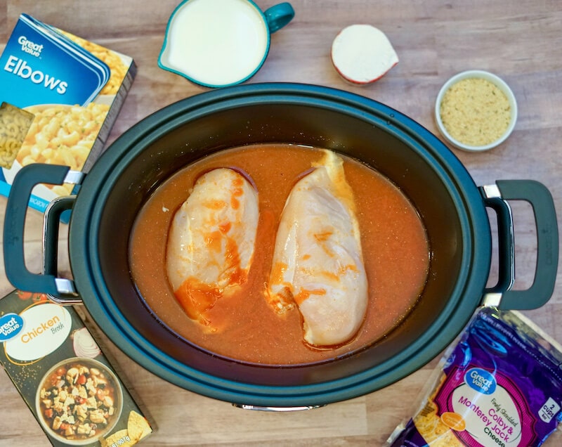 Two chicken breasts with buffalo sauce inside crock pot.