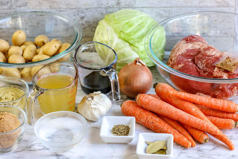 All of the ingredients for corned beef and cabbage on a white counter top.