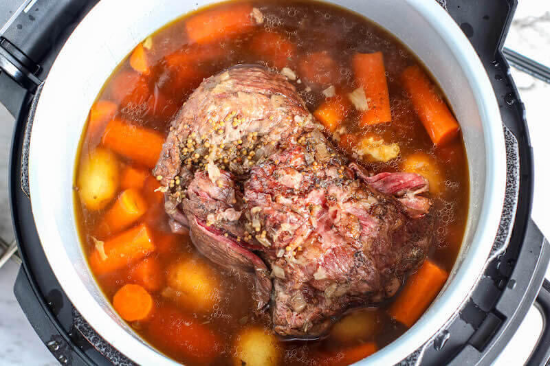 Corned beef cooked inside pot with carrots and. broth.