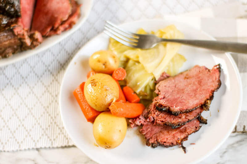 A white plate with gold potatoes, sliced carrots, cabbage, and three slices of corned beef.