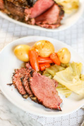 A white plate on a white tablecloth with three slices of beef, three potatoes, and a small amount of cooked cabbage.