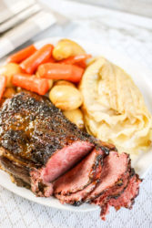 A plate of corned beef with crispy skin, cooked cabbage, and cooked carrots.