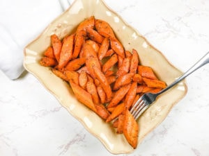 A beige serving dish filled with roasted carrots and one on a fork.