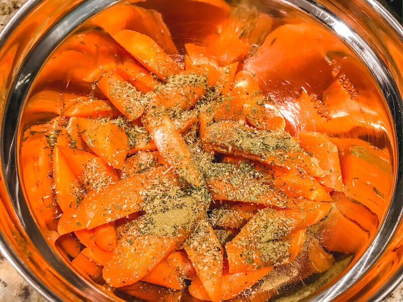 Carrots in a metal bowl and topped with oil and herbs.